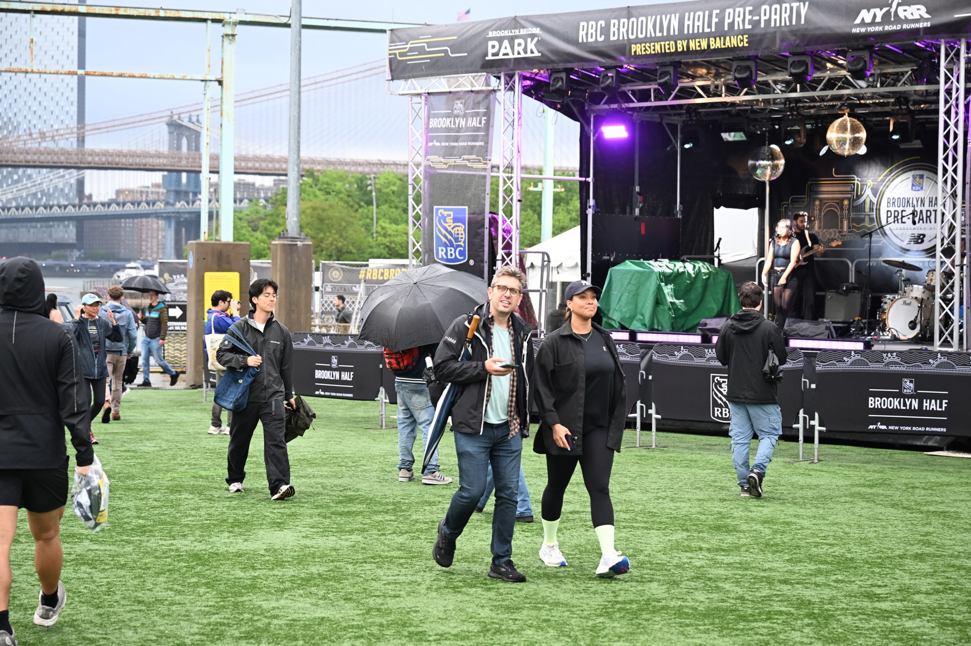 Manhattan Bridge and Brooklyn Bridge in the background as people walk around at Pier 2 at the 2025 RBC Brooklyn Half Pre-Party