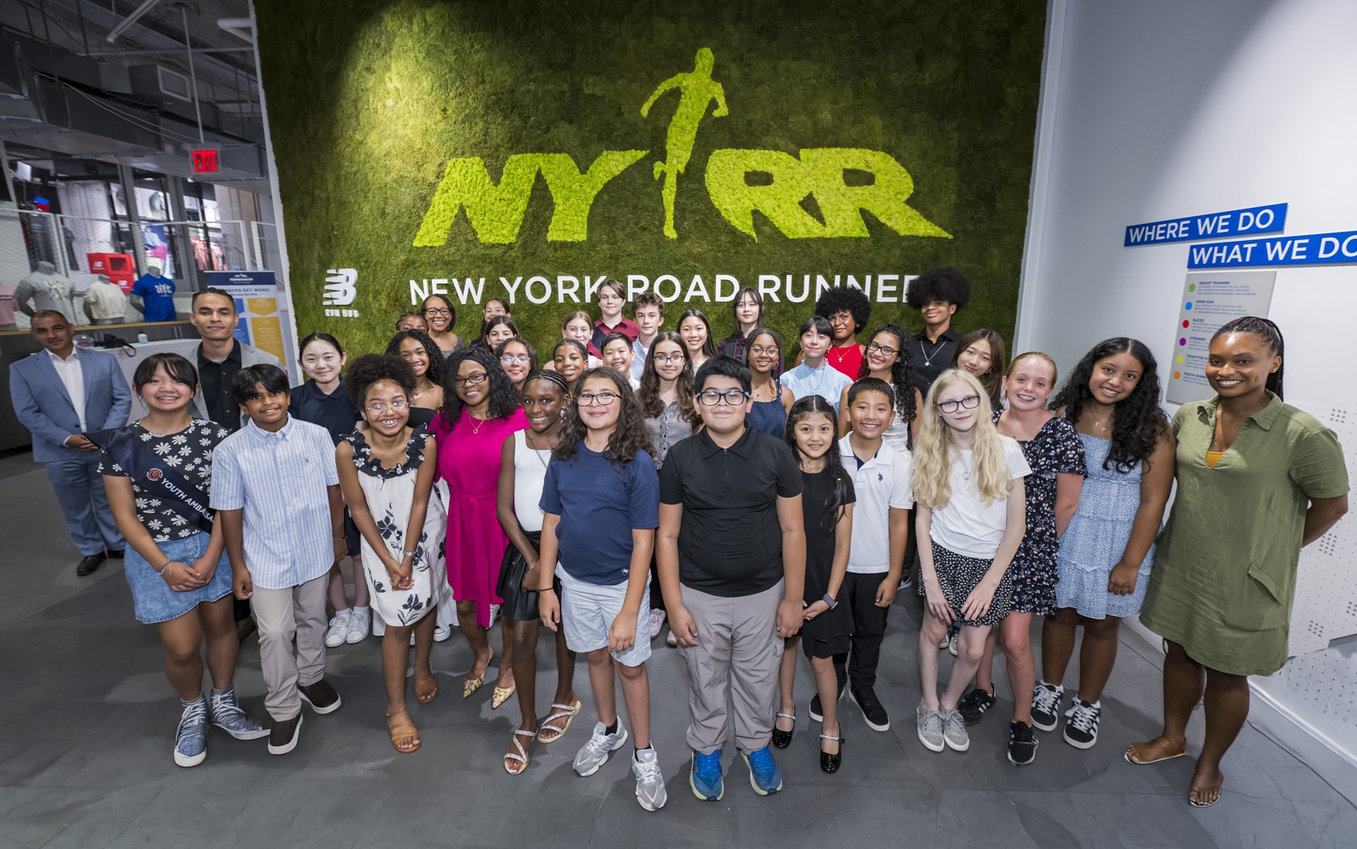 Group shot of youth ambassadors in front of a green grass wall that says NYRR New York Road Runners
