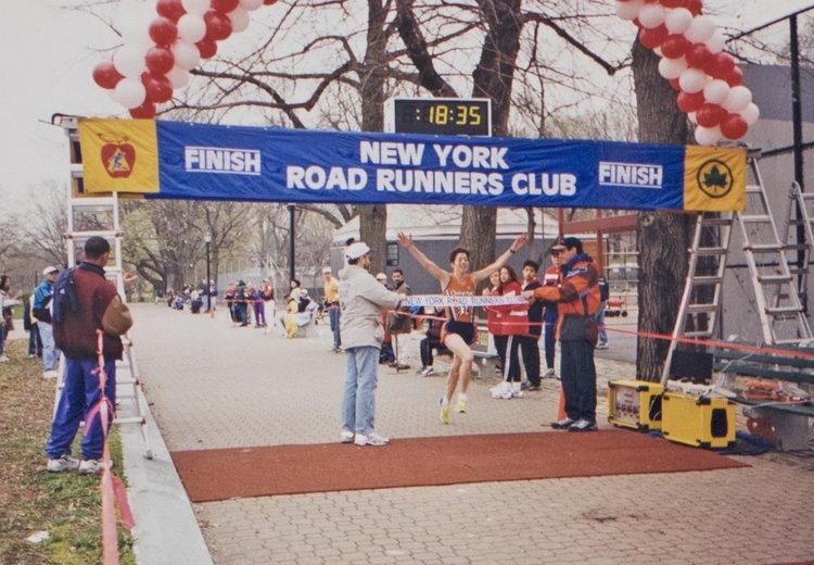 Woman runner breaking the tape at the Skaggs Walsh 5K