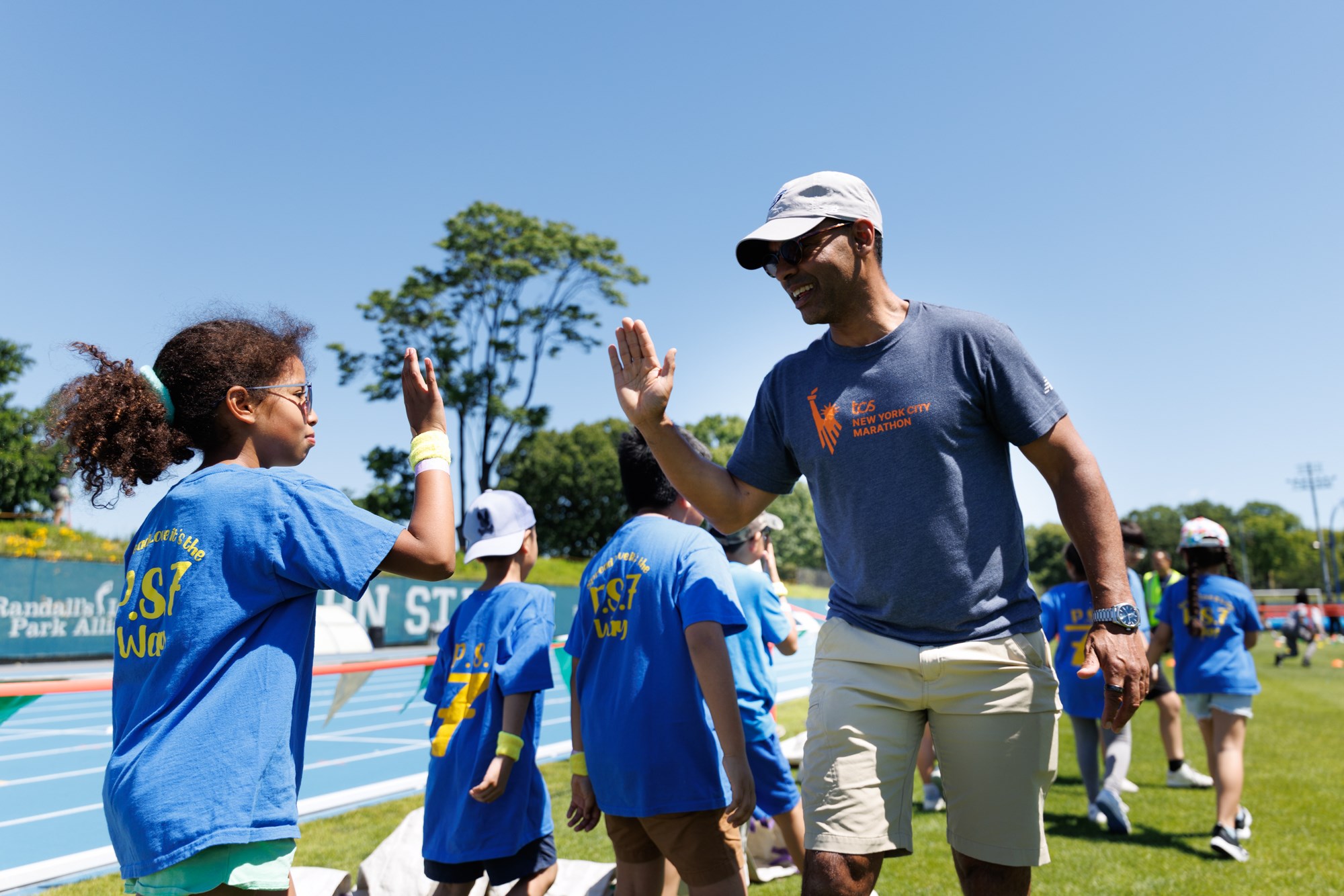 NYRR CEO Rob Simmelkjaer high fiving a child at 2026 Global Running Day at Icahn Stadium in NYC
